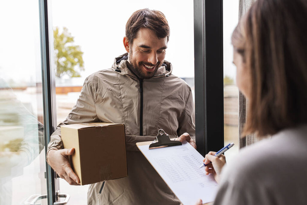 shipping, transportation and people concept - delivery man with parcel box and customer signing papers on clipboard at home - Foto, immagini