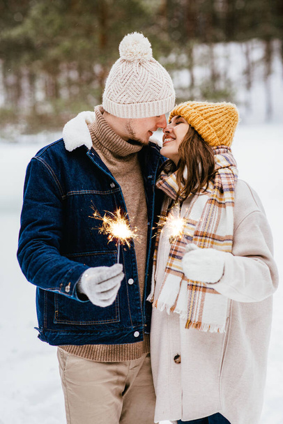 people, christmas and holidays concept - happy smiling couple with sparklers in winter forest - Zdjęcie, obraz