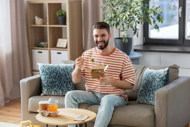 consumption, delivery and people concept - smiling man with fork eating takeaway food at home - Foto, Imagen