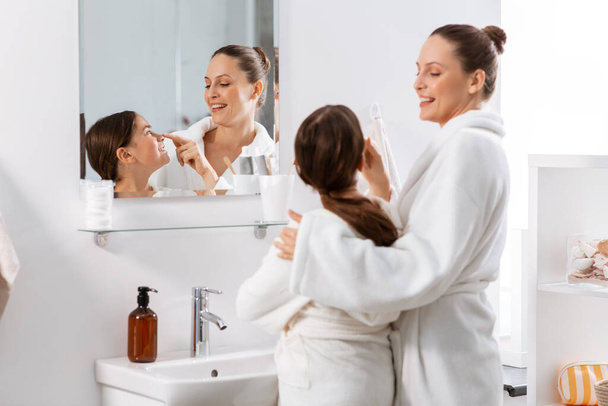 beauty, hygiene, morning and people concept - happy smiling mother and daughter in front of mirror at bathroom - Foto, imagen