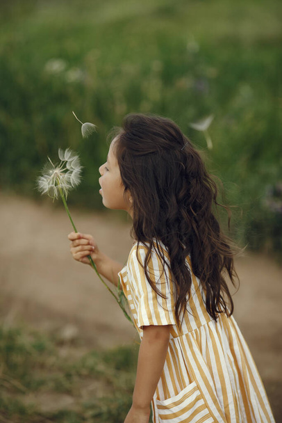 Child in a summer field. Little girl in a cute dress. - Фото, изображение