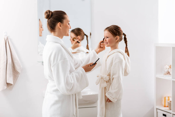 beauty, family and people concept - happy smiling mother and little daughter with brush and powder applying make up in bathroom - Fotoğraf, Görsel