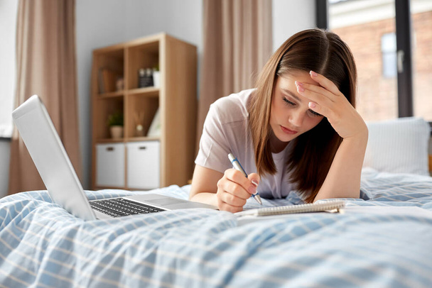 school, education and stress concept - tired teenage student girl with laptop computer and notebooks lying on bed at home - 写真・画像