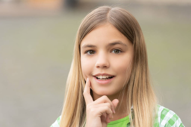 Portrait of happy teenage girl smiling with finger on cheek blurry outdoors. - Фото, зображення