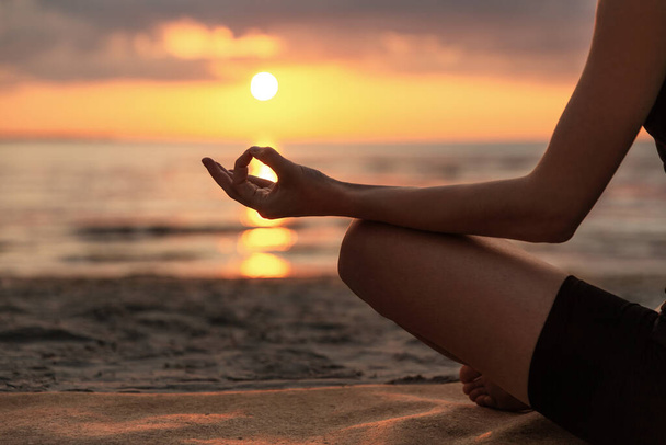 yoga, mindfulness and meditation concept - close up of woman meditating in lotus pose on beach over sunset - Valokuva, kuva