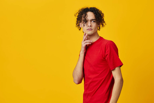 Confused funny Caucasian young man in red t-shirt can not make decision posing isolated on over yellow studio background. The best offer with free place for advertising. Emotions for everyday concept - Photo, Image