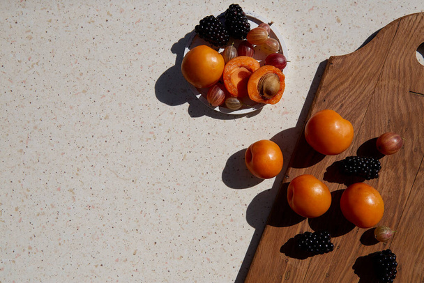 Fresh healthy summer fruits and berries - apricots, gooseberry and blackberry under hard shadows. Summer vibes. Copy space - Foto, Imagem