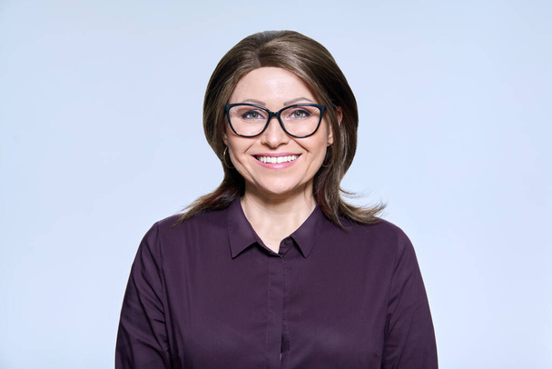 Kopfballporträt einer reifen lächelnden Frau mit Brille, die auf hellem Studiohintergrund in die Kamera blickt. Management, Personal, Beruf, Konzept für Menschen mittleren Alters - Foto, Bild