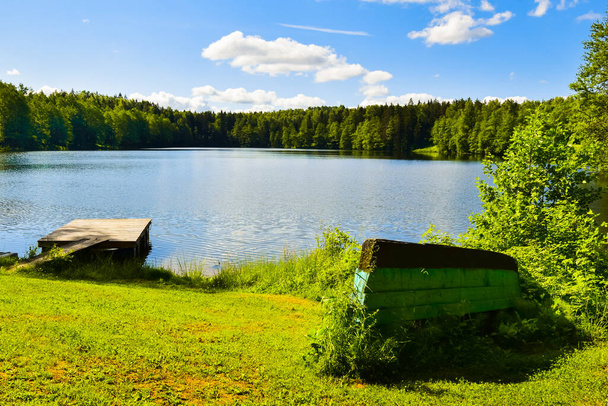 Boats upside down by calm blue lake shore in countryside of Lithuania .Fishing in baltics outdoors in summer - Photo, image