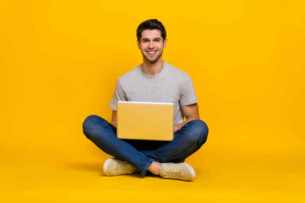 Portrait of attractive cheerful guy sitting using laptop writing email isolated over vibrant yellow color background. - Фото, зображення