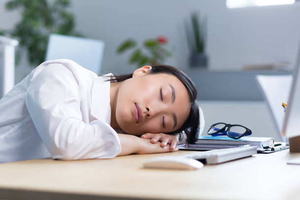 Young Asian businesswoman fell asleep at the desk on her hands in the office, tired, routine, boring work, needs a break. - Foto, imagen