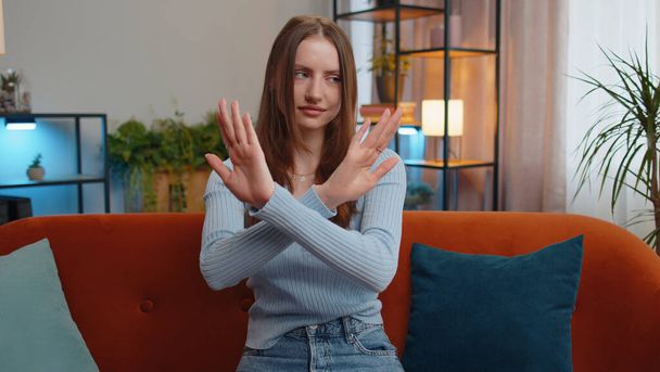 Stop gesture. Angry woman say No hold palm folded crossed hands, warning of finish, prohibited access, declining communication, body language, danger. Girl in home living room sitting on sofa indoors - 写真・画像