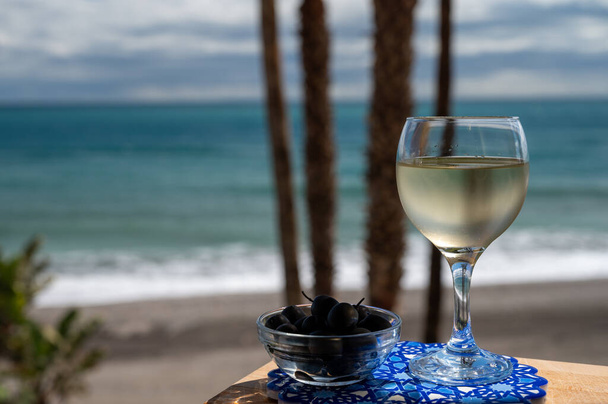 Spanish dry rueda white wine and black olives tapas served on beach terrace with view on Mediterranean sea, Andalusia, Spain - Φωτογραφία, εικόνα