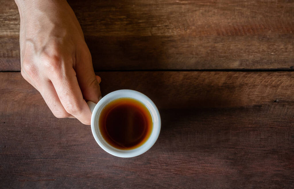 Кто-нибудь, принесите стакан черного кофе на деревянный стол. Черный кофе богат антиоксидантами, которые могут бороться с повреждением клеток и снизить риск серьезных заболеваний. - Фото, изображение