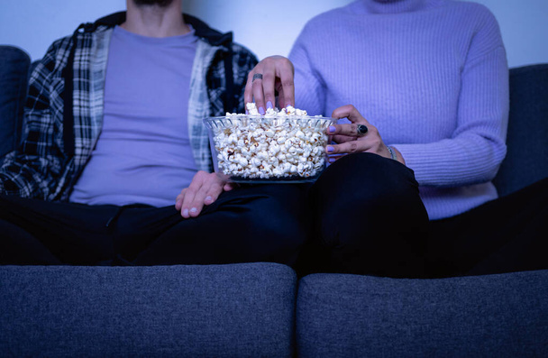 Couple eating popcorn on the couch. Unrecognizable people. Selective focus - 写真・画像