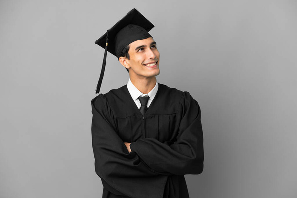Young Argentinian university graduate isolated on grey background looking up while smiling - 写真・画像