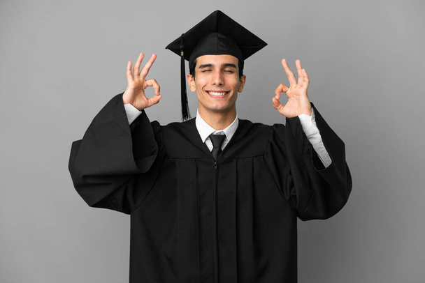 Young Argentinian university graduate isolated on grey background in zen pose - Photo, Image