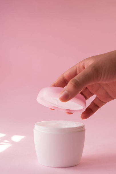 Hand opening a skin cream bottle for women on pink background - Photo, image