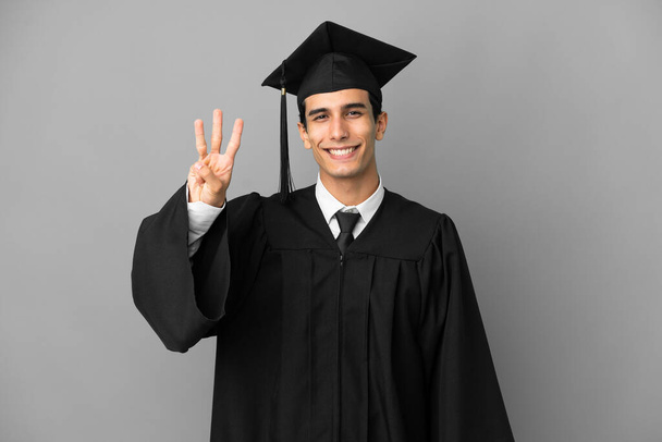 Young Argentinian university graduate isolated on grey background happy and counting three with fingers - Valokuva, kuva