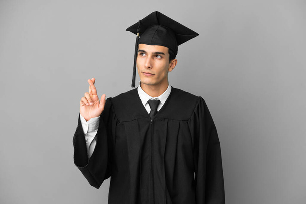 Young Argentinian university graduate isolated on grey background with fingers crossing and wishing the best - Φωτογραφία, εικόνα