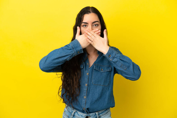 Young caucasian woman isolated on yellow background covering mouth with hands - Foto, Imagen