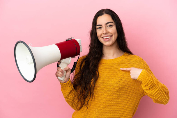 Young caucasian woman isolated on pink background holding a megaphone and with surprise facial expression - Fotoğraf, Görsel