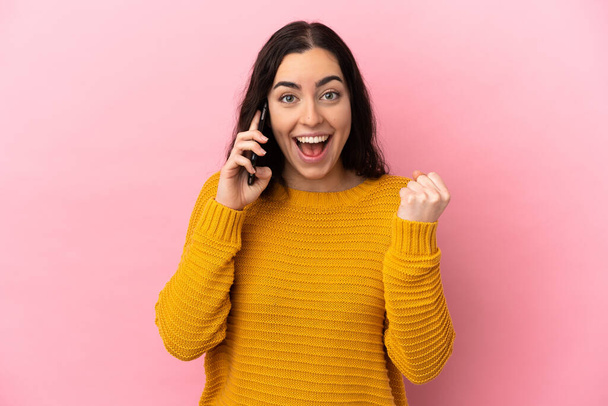 Young caucasian woman using mobile phone isolated on pink background celebrating a victory in winner position - Foto, Bild