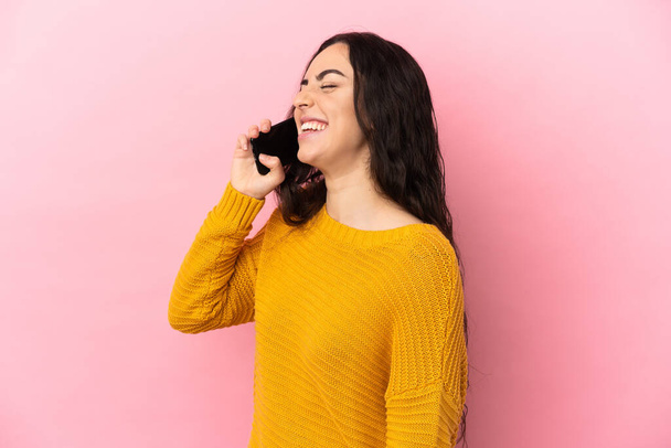 Young caucasian woman using mobile phone isolated on pink background laughing in lateral position - Foto, Imagem