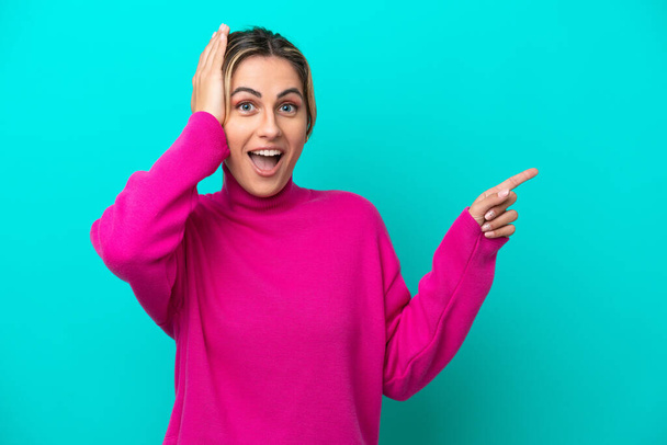 Young caucasian woman isolated on blue background surprised and pointing finger to the side - Photo, Image