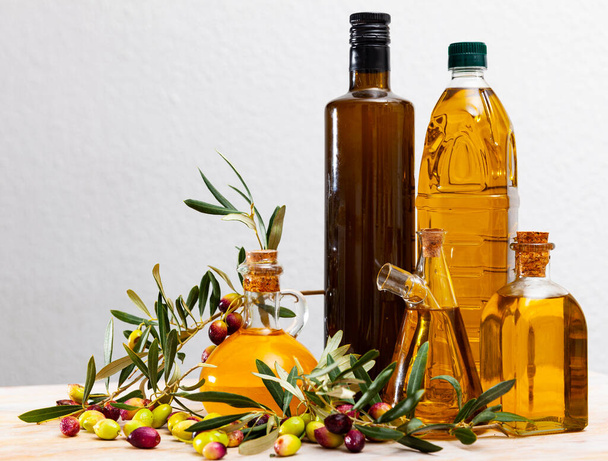 Fresh olive oil in bottles with olives on branches on wooden table - Fotografie, Obrázek