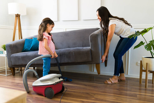 Adorable little girl helping her mother to vacuum and cleaning the dust in the living room  - Фото, зображення