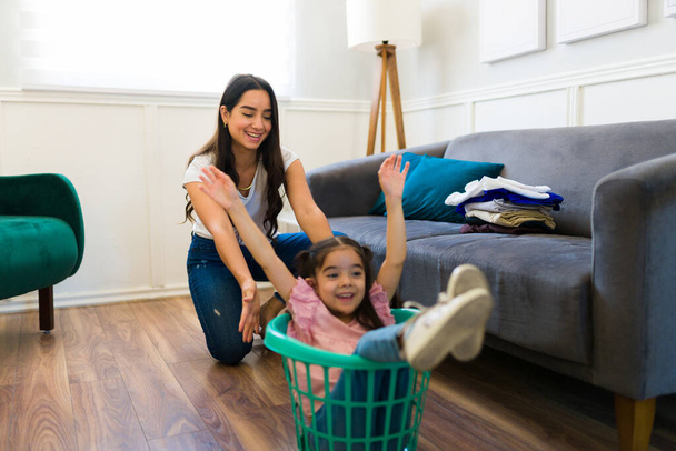 Excited mom and happy little girl playing a game while doing laundry together and having fun as a family at home - 写真・画像