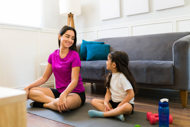 Active young mom smiling to her little daughter while exercising with yoga together in the living room - Foto, afbeelding