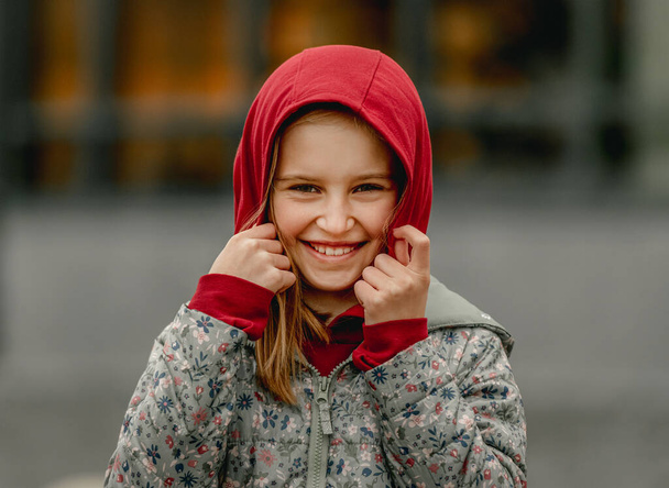 Preteen girl wearing hood at the street at autumn. Pretty female kid portrait outdoors - Photo, image
