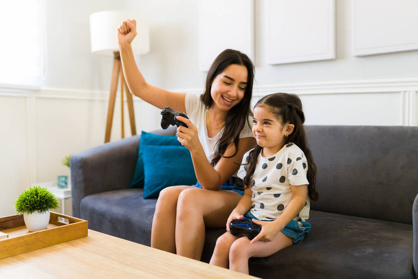 Happy mother and girl of 5 years using a remote and having fun playing video games together - 写真・画像