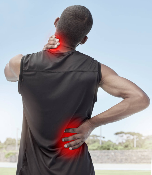 Injured and sore male runner suffering from sudden ache in his neck and back. Muscle strain or injury after a routine workout outdoors. Young sportsman struggling with unbearable pain during practice. - Foto, imagen