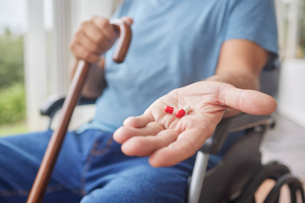 İyileşme sürecindeki hasta kıdemli adam ilaçlarını tutuyor, tekerlekli sandalyede oturuyor ve huzurevinde baston kullanıyor. Kronik hastalıklar ve hastalıklar için günlük tedavisini gören olgun bir adamın eli. - Fotoğraf, Görsel