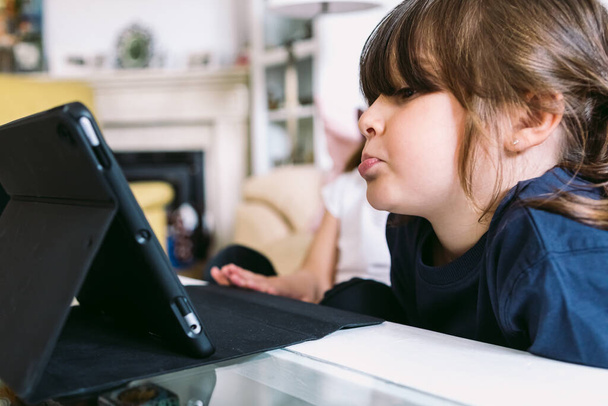 Dos niñas pequeñas mirando atentamente un video en una tableta en su sala de estar. Concepto de infancia, tecnología, aprendizaje, diversión, Internet y conectividad. - Foto, imagen