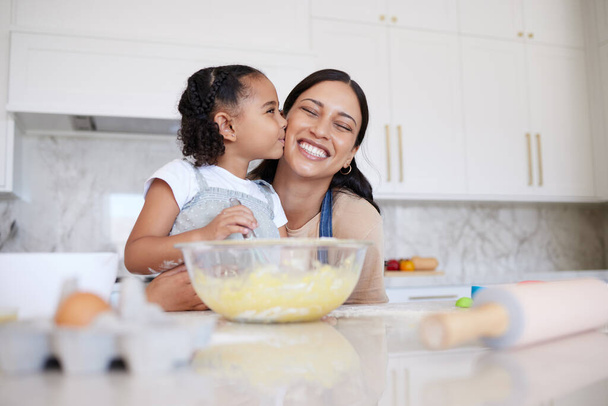 Mother and daughter baking together in a home kitchen. Caring small adorable little girl kissing her single mother on the cheek. Happy woman and affectionate child bonding inside and learning to cook. - Fotoğraf, Görsel