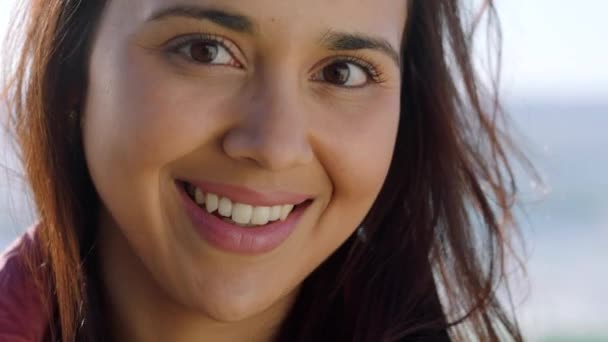 Portret van een jonge vrouw die glimlacht in het zonlicht. Mooi en aantrekkelijk brunette met een heldere, vrolijke glimlach op haar gezicht genieten van de frisse lucht buiten in een rustige en zorgeloze omgeving. - Video
