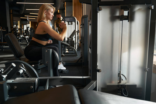 Side view of sporty woman working out on hip abduction exercise machine at gym - Foto, imagen