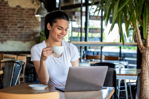 Woman in a good mood with cup of coffee sitting in cafe. Bright sunny morning. Gorgeous female drinking coffee and surfing the net in the coffee break. Morning coffee is my daily routine - Foto, Imagem