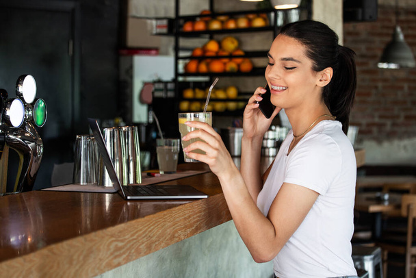 Young charming woman calling with cell telephone while sitting alone in coffee shop during free time, attractive female with cute smile having talking conversation with mobile phone while rest in bar - Foto, Imagem