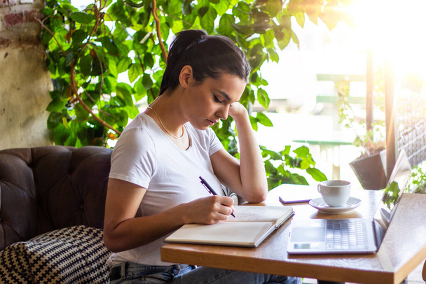 junge Frau mit süßem Lächeln sitzt mit tragbarem Netzbuch im modernen Café-Interieur während der Freizeit, charmante glückliche Studentin mit Laptop-Computer, um sich auf die Kursarbeit vorzubereiten - Foto, Bild