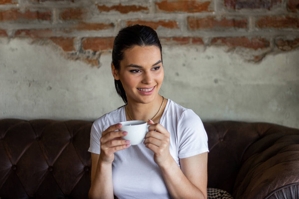 Портрет молодой женщины, пьющей кофе за столом с блокнотом в кафе, красивая симпатичная девушка в кафе у окна с улыбкой на лице - Фото, изображение