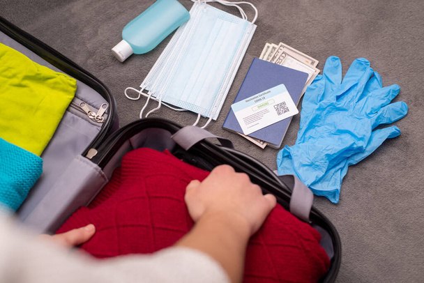 Embalaje femenino maleta de viaje con ropa, documentos, cosas de higiene personal. Viajero que va a un viaje después de la vacunación con Covid-19. - Foto, Imagen
