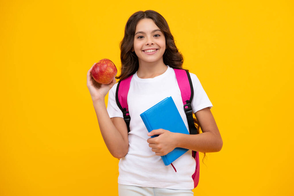 Criança escolar, estudante adolescente menina com bagpack segurar maçã e livro isolado em amarelo - Foto, Imagem