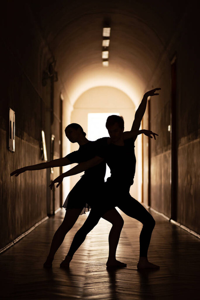 Силуэты элегантной пары артистов балета. Танцевать в коридоре с высоким потолком. - Фото, изображение