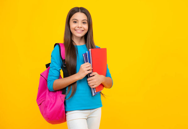 Happy teenager portrait. Schoolgirl, teenage student girl hold book on yellow isolated studio background. School and education concept. Back to school. Smiling girl - Foto, immagini
