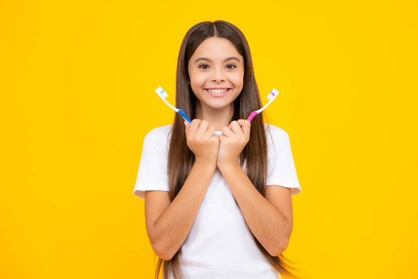 Happy teenager portrait. Portrait of caucasian teen girl holds a toothbrush brushing her teeth, morning routine, dental hygiene, isolated on yellow background. Smiling girl - Zdjęcie, obraz
